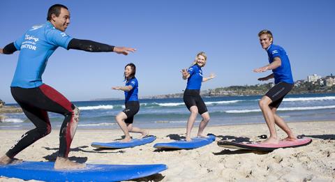 본다이 비치에서 '레츠고 서핑(Let's Go Surfing)' 강사에게 서핑을 배우고 있는 젊은 여자 둘과 젊은 남자 하나